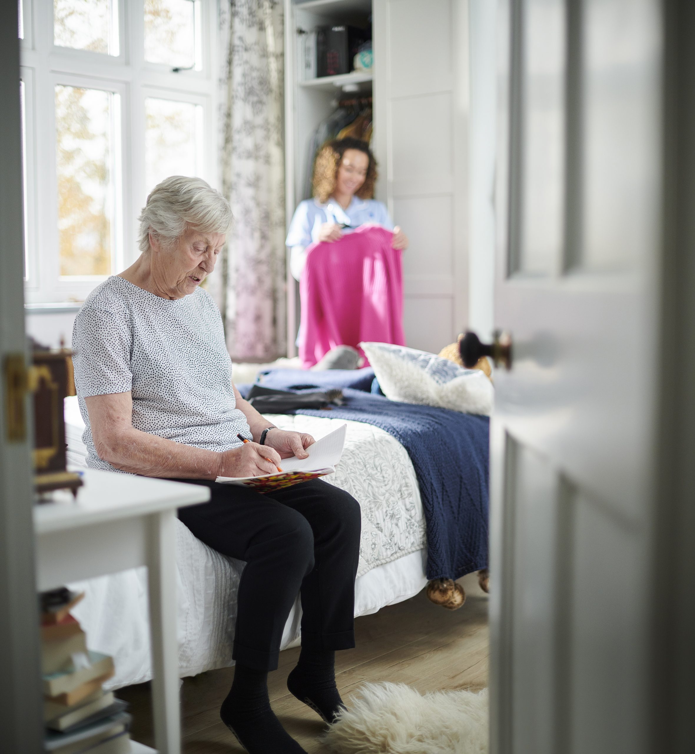 home carer helping senior woman get dressed in her bedroom